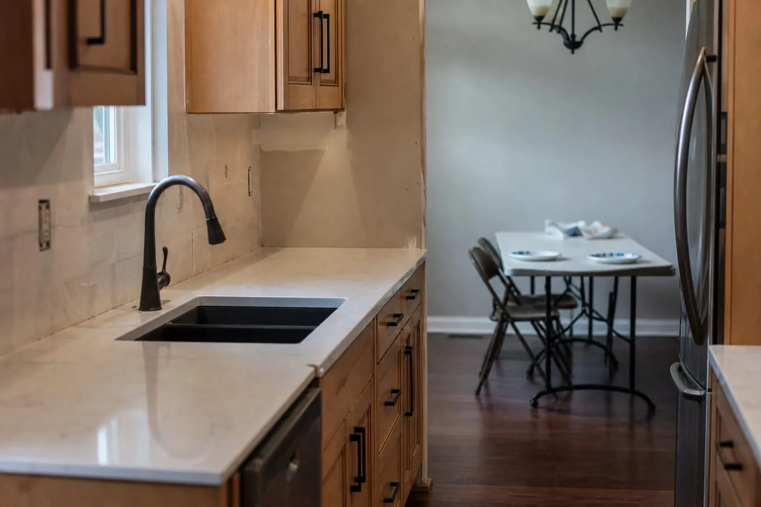 A partially finished galley kitchen with new cabinets installed, a quartz countertop with a visible seam near the sink, bare wall where a backsplash would go...